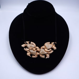 May include: A necklace featuring a cluster of carved turtle shells in a light brown color. The turtles are arranged in a symmetrical pattern, creating a unique and eye-catching design.