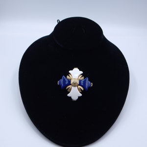 May include: A white and blue enamel cross brooch with a gold center and a small rhinestone in the center.