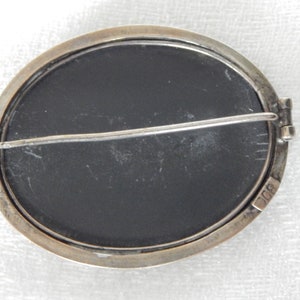 Puede incluir: Un broche ovalado de plata con un camafeo negro. La parte posterior del broche tiene un pasador de plata y un cierre. El broche est&aacute; marcado con "900" en la parte posterior.