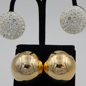 May include: A pair of earrings, one with a gold ball and the other with a white ball covered in rhinestones.