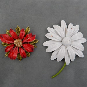 May include: Two vintage metal flower brooches. One is a red poinsettia with gold accents and the other is a white daisy with a green stem.