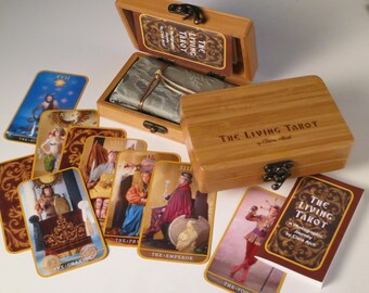 May include: A wooden box with a set of tarot cards. The box is labeled "The Living Tarot" and the cards feature illustrations of people in various poses. The cards are laid out on a white surface.