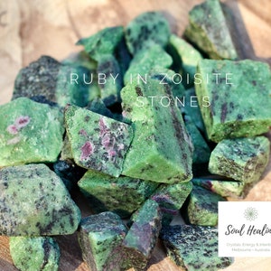 May include: A pile of raw ruby in zoisite stones. The stones are a vivid green colour, with dark grey and red flecks. The text "RUBY IN ZOISITE STONES" is displayed in white. The image also includes a logo for "Soul Healing".