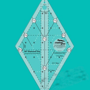 Puede incluir: Una regla de acolchado transparente en forma de diamante con marcas y medidas en negro. La regla presenta el texto "60° Diamond Tiny" y "Designed by Krista Moser". Incluye medidas en pulgadas, como 1 1/2" Hex, 2 1/2" Hex y 3 1/2" Hex.