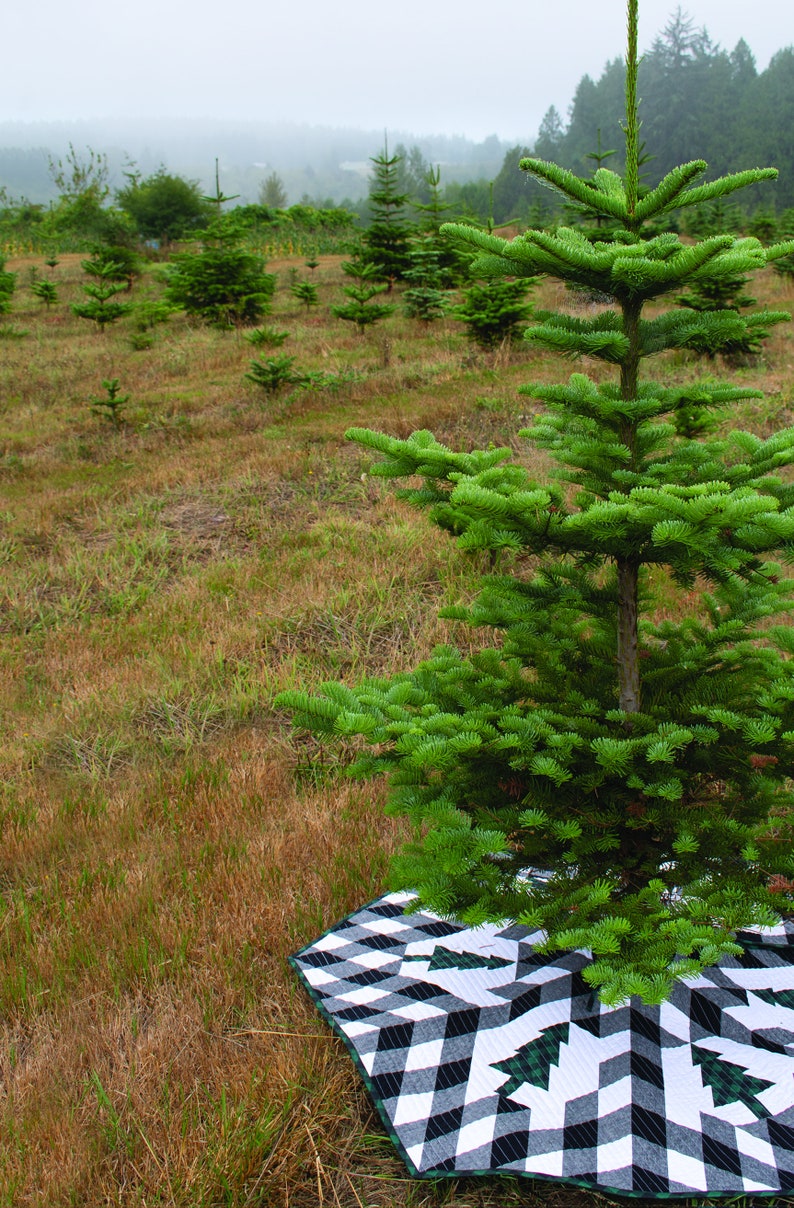 Puede incluir: Un &aacute;rbol de Navidad verde con una falda de &aacute;rbol con estampado de copo de nieve en blanco y negro. El &aacute;rbol est&aacute; en un campo con otros &aacute;rboles en el fondo.