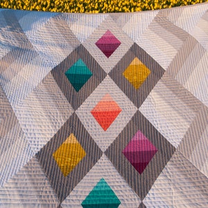 Puede incluir: Una colcha con un patr&oacute;n geom&eacute;trico de diamantes grises y blancos. Los diamantes est&aacute;n rellenos de patrones de degradado de colores en tonos de rosa, naranja, amarillo, turquesa y morado.