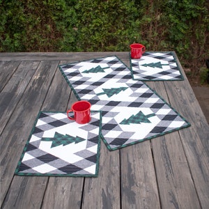 Puede incluir: Tres tazas rojas sobre un juego de tres manteles individuales acolchados verde y blanco con un patr&oacute;n geom&eacute;trico. Los manteles individuales presentan un dise&ntilde;o estilizado de &aacute;rbol de Navidad verde. Los manteles individuales est&aacute;n sobre una mesa de madera.