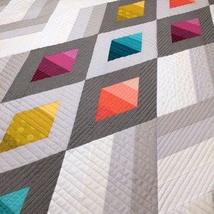 Puede incluir: Una colcha con un patr&oacute;n geom&eacute;trico de diamantes grises y blancos. Los diamantes est&aacute;n delineados en gris y rellenos de tela degradada de colores en tonos de amarillo, naranja, rojo, rosa, azul y turquesa.