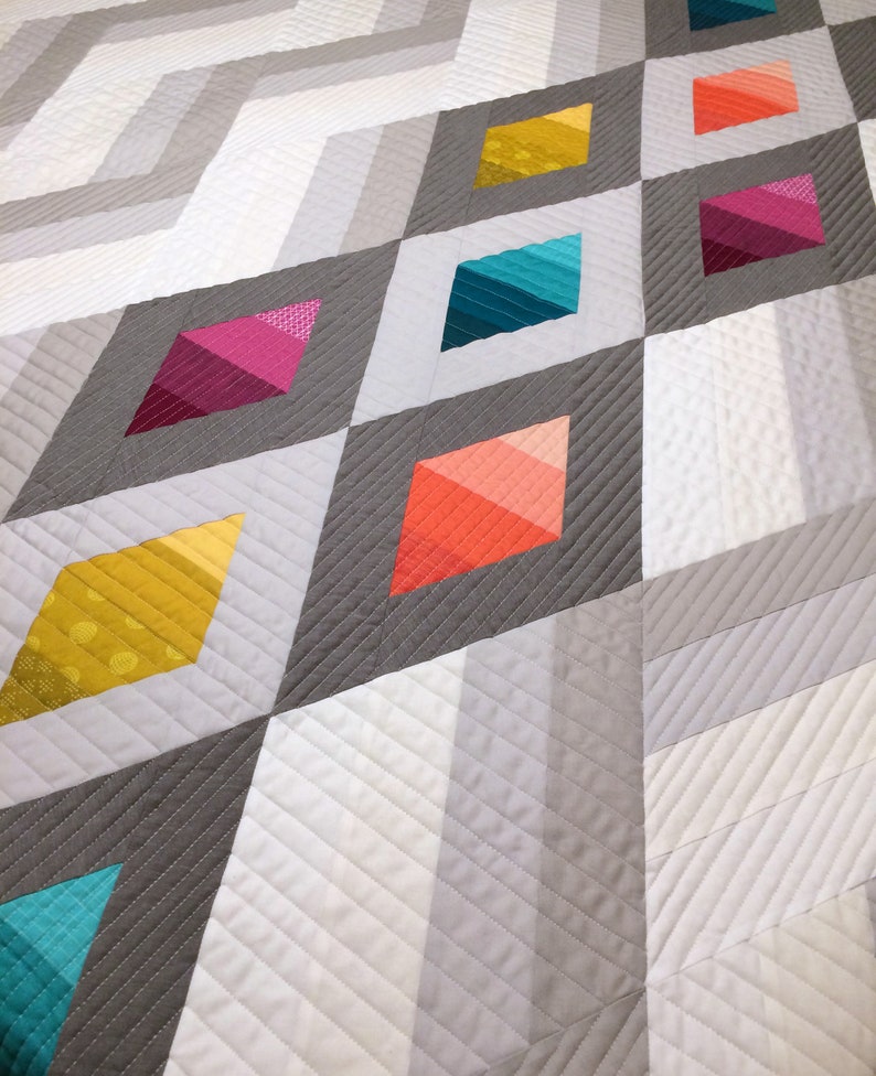 Puede incluir: Una colcha con un patr&oacute;n geom&eacute;trico de diamantes grises y blancos. Los diamantes est&aacute;n delineados en gris y rellenos de tela degradada de colores en tonos de amarillo, naranja, rojo, rosa, azul y turquesa.