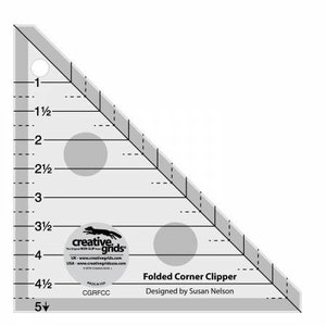May include: A clear, triangular quilting ruler with black markings and measurements in inches. The ruler has a rounded corner and two gray circles. Text on the ruler includes "Folded Corner Clipper" and "Designed by Susan Nelson."