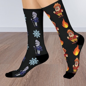 May include: A pair of black socks with a winter and summer theme. One sock features a snowflake pattern and a cartoon character with a microphone. The other sock features a cartoon character with flames and a microphone.