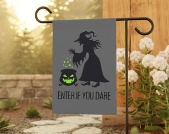 May include: A gray garden flag with a black witch silhouette, a cauldron with a green glowing face, and the text "ENTER IF YOU DARE." The flag is displayed on a black metal stand in a garden setting.