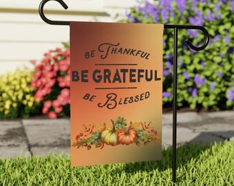 May include: A garden flag with a fall theme. It has a gradient background of orange and yellow with the text "Be Thankful, Be Grateful, Be Blessed". There are two pumpkins and fall leaves in the bottom of the flag.