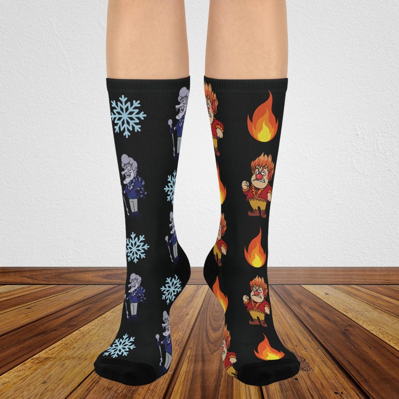 May include: A pair of black crew socks featuring a mismatched design. The left sock displays light blue snowflakes and a cartoon character with white hair. The right sock features orange and yellow flames and a cartoon character with red hair.