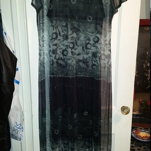 May include: A black and white sheer mesh dress with a floral pattern. The dress has a scoop neck and short sleeves. The dress is layered over a black slip dress with a floral pattern.