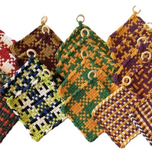 May include: A collection of woven potholders in various colors, including red and white, green and orange, and purple and gold. Each potholder has a square shape with a wooden ring for hanging. The woven design creates a textured appearance.