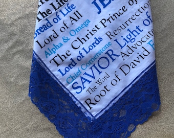 Könnte beinhalten: Ein weißes Stoffquadrat mit blauer Spitzenborte. Der Stoff hat blauen und schwarzen Text, der "ay, N The Life Bread of Life Lord of All JESUS Alpha & Omega The Christ Prince of Life Lord of Lords Resurrection Chief Cornerstone SAVIOR Light of The Word Root of David F" lautet.