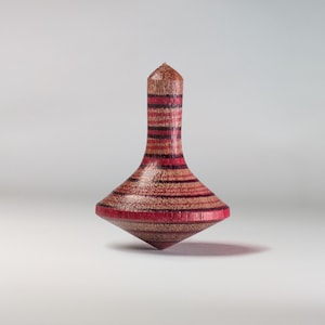 May include: A wooden spinning top with red and brown stripes. The top is pointed at the top and has a rounded base.