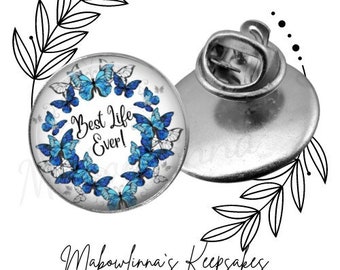 May include: A silver pin with a blue and white glass cabochon featuring a butterfly design and the text "Best Life Ever!"