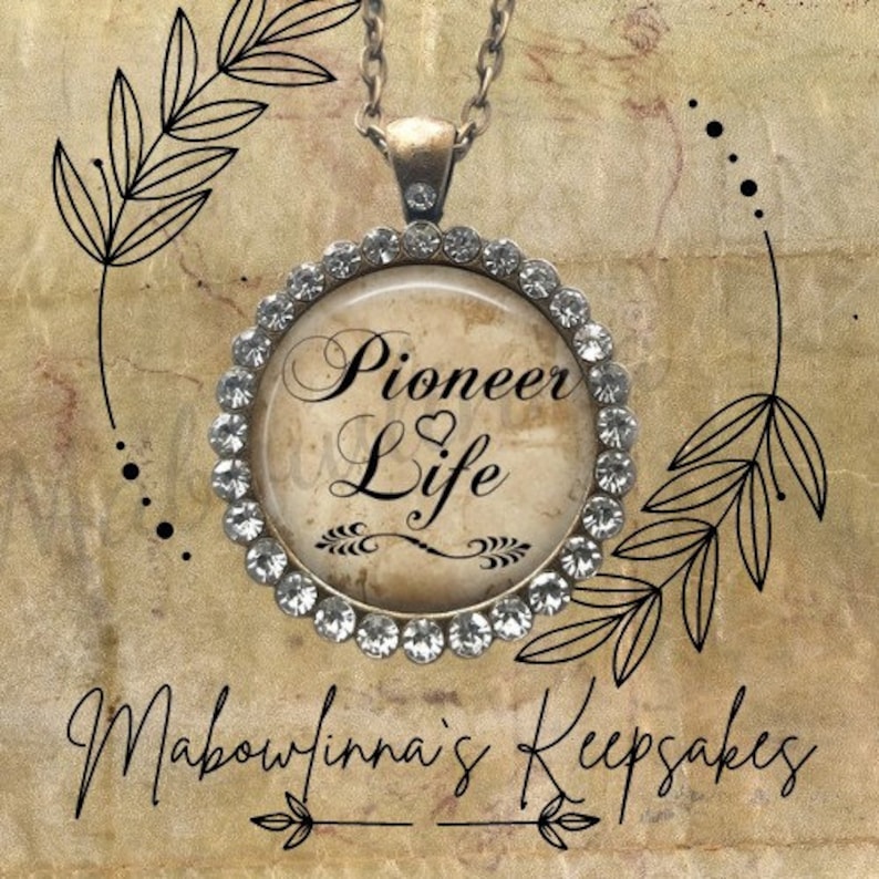 May include: A round pendant necklace with the words "Pioneer Life" in elegant script. The pendant is surrounded by a ring of clear crystals and hangs from a silver chain. The background is a textured, sepia-toned surface with decorative leaf illustrations.