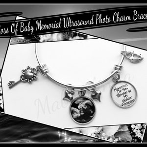 Op de afbeelding: Een zilveren armband met een kleine sleutel, een hart, een bloem, een hart, een echografiefoto en een ronde bedel met de tekst "Memories of you remain in my heart forever".