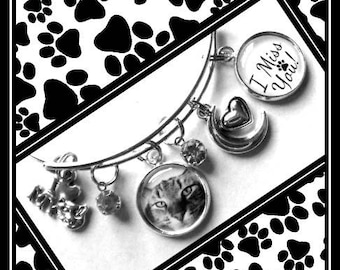 Könnte beinhalten: Ein silbernes Armband mit einem Pfotenabdruck-Anhänger, einem Katzen-Anhänger, einem Herz-Anhänger, einem Halbmond-Anhänger und einem runden Anhänger mit dem Text "I Miss You!"