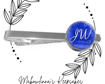 May include: A silver tie bar with a blue glass circle featuring the initials "JW" in white script.
