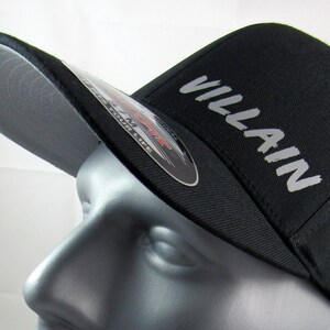 May include: A black baseball cap with a gray brim and the word "VILLAIN" embroidered in white on the front.