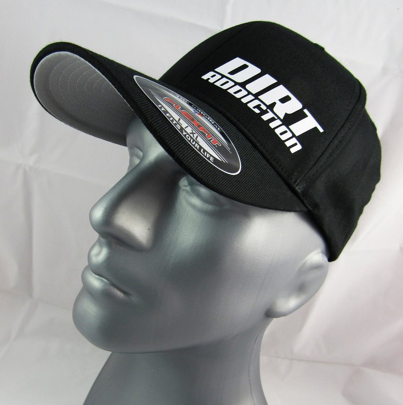 May include: A black baseball cap with a white logo that says "Dirt Addiction". The cap has a grey underbill and a Flexfit label.