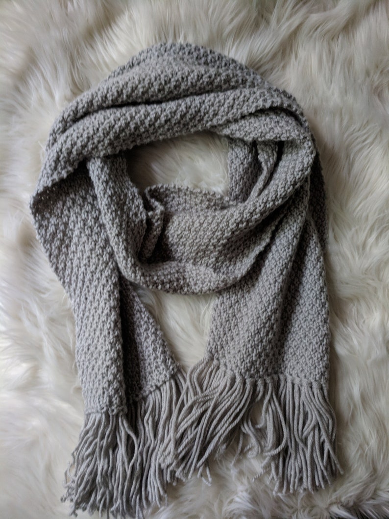 Knit scarf in the double moss stitch laid flat with fringe details on the end.