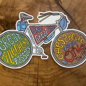 May include: A colorful sticker of a bicycle with the words "One Great Ride" on the frame. The wheels are decorated with the names of different bike trails: "Great Allegheny Passage" and "Chesapeake and Ohio Tow Path".