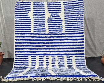 Puede incluir: Alfombra rectangular a rayas azules y blancas con diseño geométrico. La alfombra tiene flecos en el borde inferior. Se muestra sobre un fondo neutro. Ideal para salón o dormitorio.