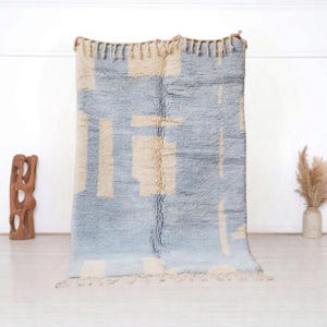 Peut inclure: Un tapis marocain bleu clair et crème avec un motif géométrique. Le tapis a une bordure à franges.