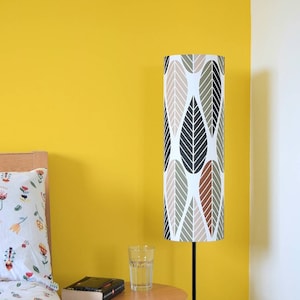 May include: A bedroom with a yellow wall, a white wall, a bed with a floral patterned duvet cover, a side table with a book and a glass of water, and a floor lamp with a leaf patterned lampshade.