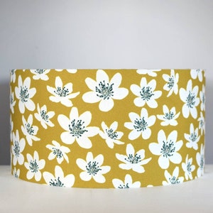May include: A yellow lampshade with a white floral pattern. The flowers have a green center.