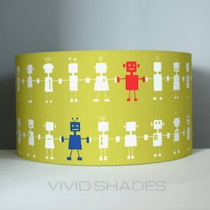 May include: A cylindrical lampshade with a light green background. The lampshade is decorated with a repeating pattern of white robot figures holding hands. Two robots are colored red and blue. The text "VIVID SHADES" is at the bottom.