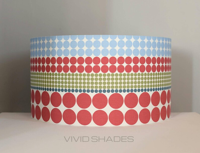 May include: A cylindrical lampshade with a geometric pattern of red, blue, and green circles. The lampshade is made of fabric and has a white background.