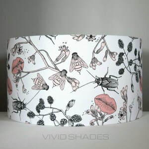 May include: A white lampshade with a black and pink floral pattern featuring insects, leaves, and flowers. The lampshade has a pink lip design.