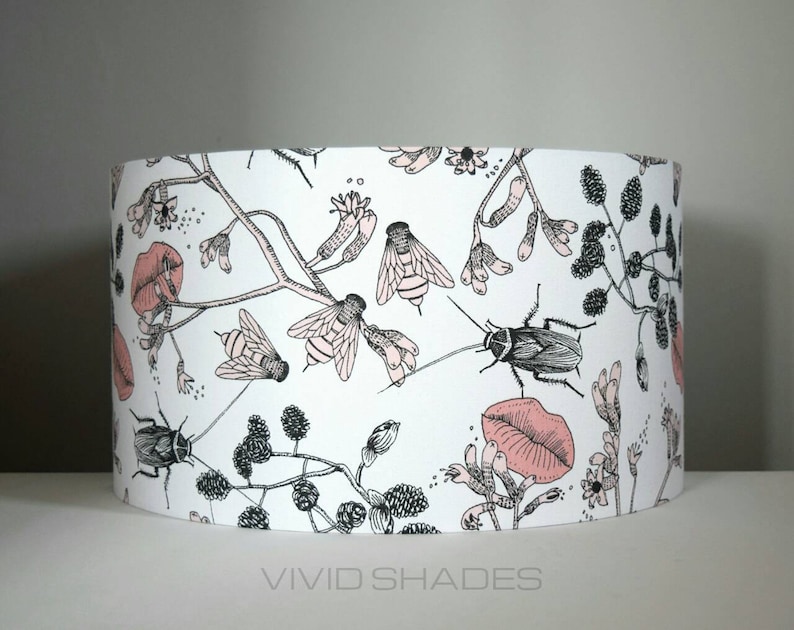May include: A white lampshade with a black and pink floral pattern featuring insects, leaves, and flowers. The lampshade has a pink lip design.