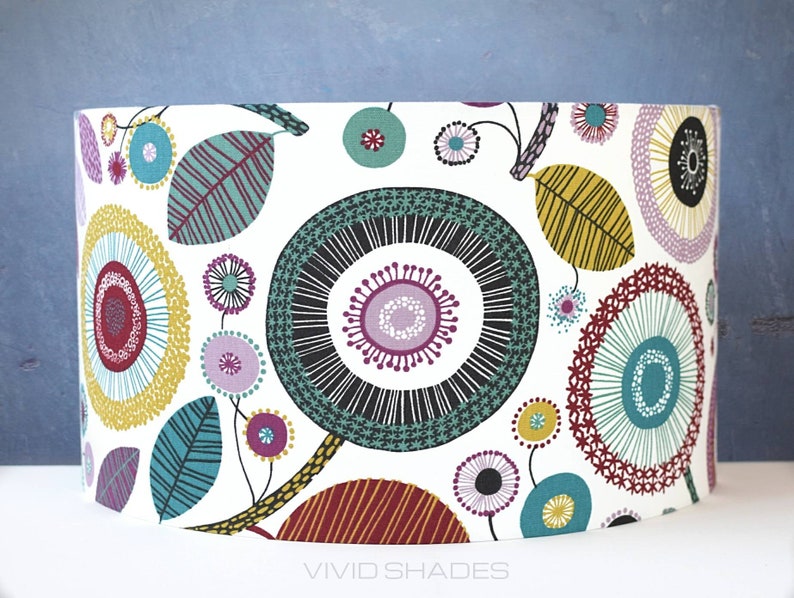 May include: A white drum lampshade with a colorful geometric pattern of circles, leaves, and dots in shades of teal, yellow, red, purple, and black. The pattern is reminiscent of a modern floral design.