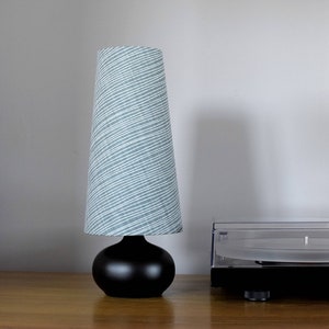 May include: A black table lamp with a grey and white patterned lampshade. The lamp is sitting on a wooden table next to a black record player.