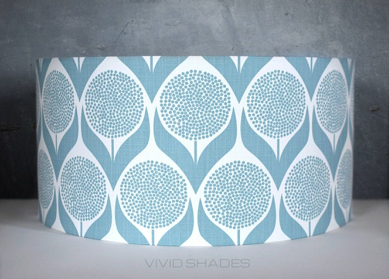 May include: A blue and white patterned lampshade with a repeating design of stylized flowers. The lampshade is cylindrical and has a white background with blue flowers.