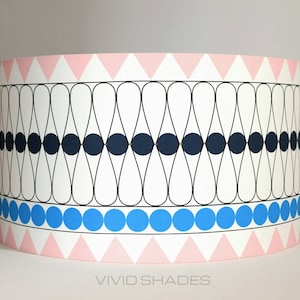 May include: A white lampshade with a geometric pattern of pink triangles, black circles, and blue circles. The lampshade has a black and white pattern of teardrop shapes.