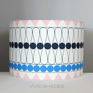 May include: A white lampshade with a geometric pattern of black ovals and circles, a blue band of circles, and a pink band of triangles. The lampshade has the text "VIVID SHADES" printed on the bottom.