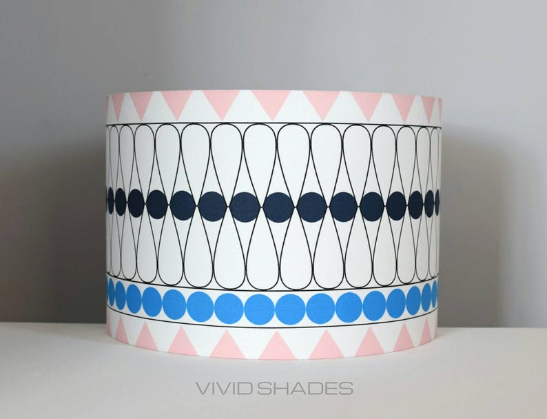 May include: A white lampshade with a geometric pattern of black ovals and circles, a blue band of circles, and a pink band of triangles. The lampshade has the text "VIVID SHADES" printed on the bottom.