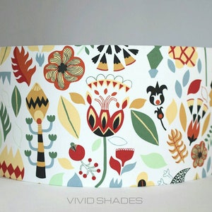 May include: A white lampshade with a colorful floral pattern. The pattern features red, yellow, green, and black flowers and leaves. The lampshade is labeled "VIVID SHADES".