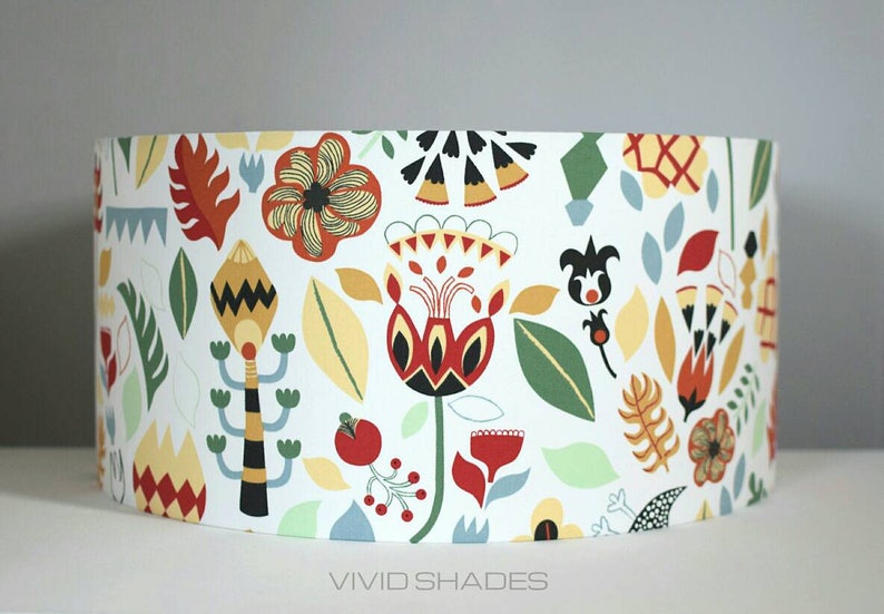 May include: A white lampshade with a colorful floral pattern. The pattern features red, yellow, green, and black flowers and leaves. The lampshade is labeled "VIVID SHADES".