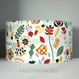May include: A white lampshade with a colorful floral and geometric pattern. The pattern includes red, yellow, green, blue, and black. The lampshade is cylindrical and has a white background.
