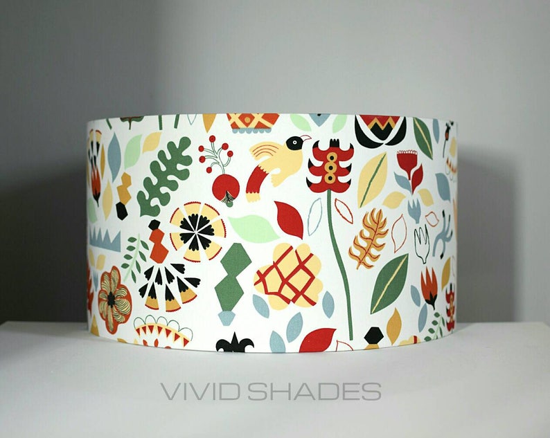 May include: A white lampshade with a colorful floral and geometric pattern. The pattern includes red, yellow, green, blue, and black. The lampshade is cylindrical and has a white background.