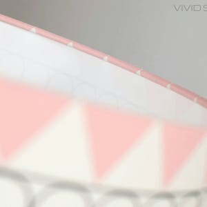May include: A pink and white lampshade with a geometric pattern of triangles. The lampshade is made of fabric and has a white lining.